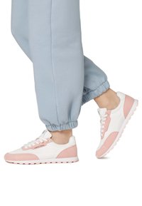 Sneaker atletiche bianche e rosa chiaro con una tomaia in camoscio e rete, punta arrotondata e suola imbottita, abbinate a pantaloni jogger blu chiaro.