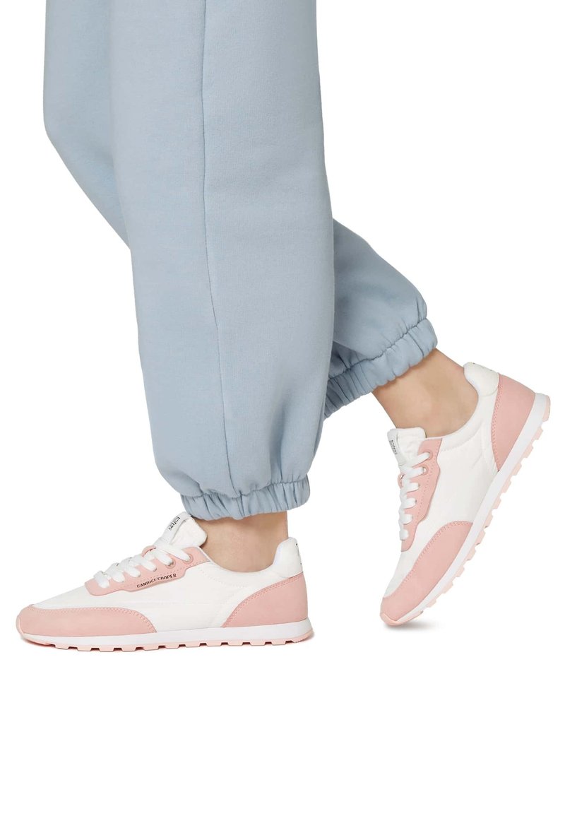 Sneaker atletiche bianche e rosa chiaro con una tomaia in camoscio e rete, punta arrotondata e suola imbottita, abbinate a pantaloni jogger blu chiaro.