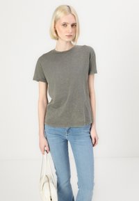 Gray, short-sleeve t-shirt made of soft fabric with a slight texture. Paired with light blue jeans and a white handbag.