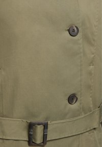 Světlý olivově zelený kabát se dvěma tmavými knoflíky a páskem ze stejné látky s tmavou obdélníkovou sponou.