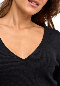 Maglione nero a costine con scollatura a V profonda e una finitura testurizzata con accenti metallici. Primo piano dei dettagli del tessuto e della scollatura.