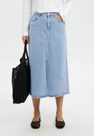 Gonna in denim azzurro chiaro con taglio dritto, chiusura frontale con bottoni e tasche laterali. Abbinata a una borsa a tracolla nera intrecciata e scarpe in rete.