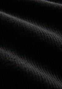 Tessuto di velluto a coste nero con una texture a coste, caratterizzato da fibre sottili e morbide che creano un aspetto liscio. Colorazione uniforme in tutto il tessuto.