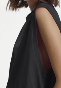 Svart ärmlös topp med breda ärmhålor, slät yta och minimalistisk design. Har rund halsringning och subtila draperingar.