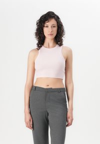 Svijetloružičasti rebrasti crop top s visokim izrezom, uparen s tamno sivim krojenim hlačama koje imaju glatku teksturu i prednje džepove.