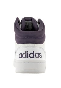 Zapatilla alta de Adidas con base de cuero blanco y cuello de textil púrpura. Presenta un logotipo en el talón y una suela de goma texturizada.