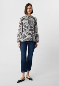 Bluse mit floralem Muster in Hellgrau mit schwarzen Akzenten, lange Ärmel, runder Halsausschnitt, kombiniert mit dunkelblauen, ausgestellten Jeans.