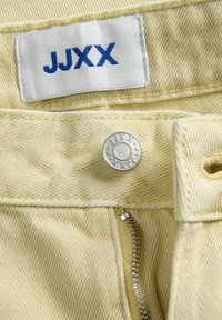 Μπεζ τζιν από τζιν με μερικώς ανοιχτό μεταλλικό φερμουάρ, μεταλλικό κουμπί με λογότυπο και λευκή υφασμάτινη ετικέτα με μπλε κείμενο "JJXX".