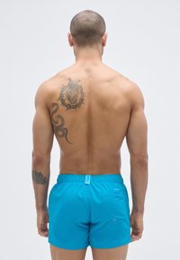 Calções de banho turquesa com cintura elástica, bolso traseiro e detalhes contrastantes em azul; apresentam um material suave e leve.