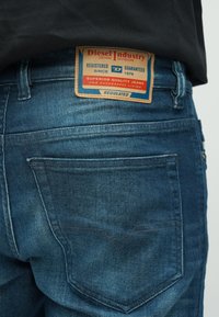 Keskmise sinise tooniga teksapüksid, millel on nahast tagumine märk "Diesel Industry". Omavad kahte tagataskut ja peeneid õmblusdetailsusi.