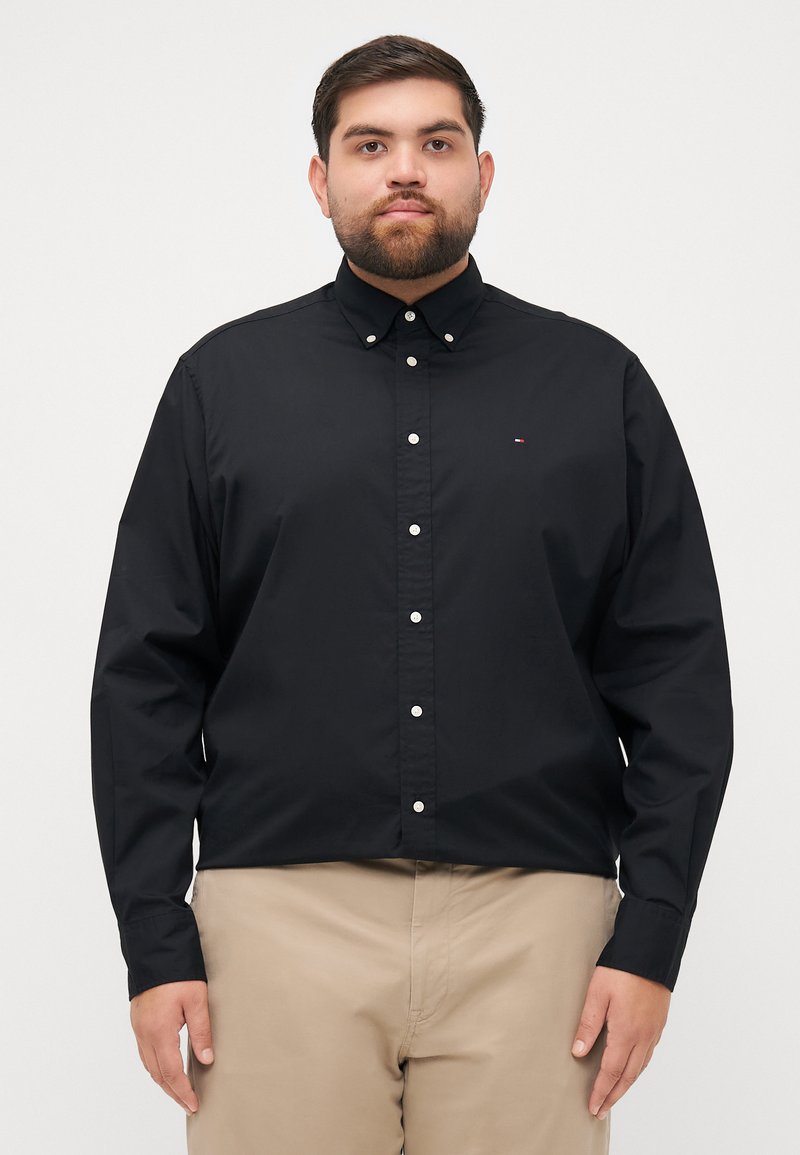 Black button-up shirt with long sleeves, featuring a pointed collar and white buttons, made from smooth fabric. Small logo on the chest.