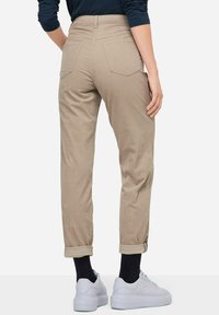 Pantaloni beige a vita alta con risvolti, cinque tasche e una texture liscia. Indossati con sneakers bianche e calzini neri alla caviglia.