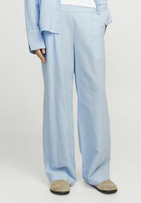 Gaišu zilu svītrainu platā kāja bikses, izgatavotas no gludas auduma ar brīvu piegriezumu. Redzamās sānu kabatas un kontrastējoši gaišie raksti.