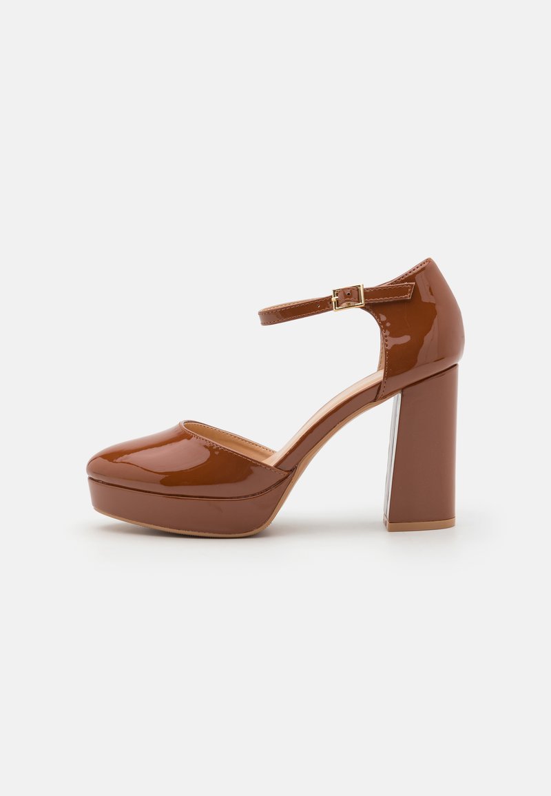 Escarpin en cuir verni marron avec un bout rond, une sangle de cheville et un talon bloc épais. Présente un accent de talon transparent.