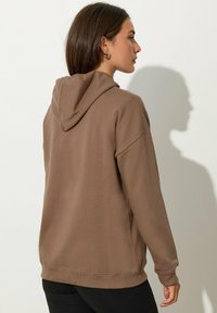 Felpa con cappuccio marrone, dal taglio rilassato, con polsini e orlo a costine. Realizzata in tessuto morbido, presenta un design semplice e senza motivi visibili.