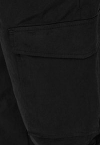 Černé cargo šortky mají boční kapsu se klopou, vyrobené z odolné tkaniny s jemnou strukturou a čistými švy.