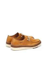 Zapatos de cuero marrón con un acabado suave, punta redondeada, diseño de cordones y una suela texturizada en color crema. Presenta detalles cosidos y una marca.