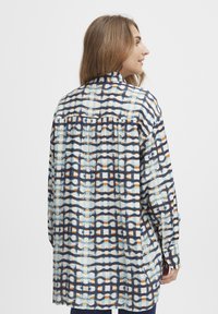Camisa abotonada de tejido ligero, con un patrón geométrico en azul, blanco y naranja. Mangas largas, corte relajado, de longitud media.