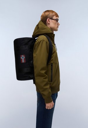 Mochila cilíndrica negra con un parche de la bandera noruega, hecha de material resistente, llevada por una persona con chaqueta verde y vaqueros azules.