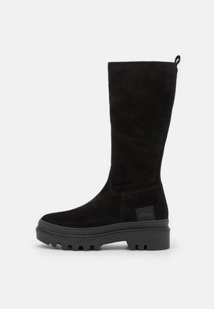 Czarny zamszowy but do połowy łydki z grubą podeszwą z protektorem, zaokrąglonym noskiem i pętelką u góry z tyłu, boczna naszywka z logo w pobliżu kostki.