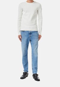 Valkoinen pitkähihaisessa ribbipaitassa, joka on yhdistetty vaaleansiniisiin suoriin farkkuihin ja mustiin puukengiin. Minimalistinen muotoilu, tiukka siluetti.