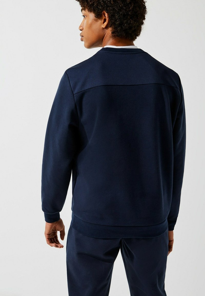 Sweatshirt en polaire marine présentant un panneau texturé au dos supérieur, des poignets et un ourlet côtelés. Tissu lisse avec une coupe décontractée.
