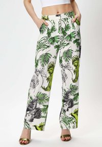 White wide-leg pants with green and black tropical leaf and bird print, featuring side pockets and a flat waistband.