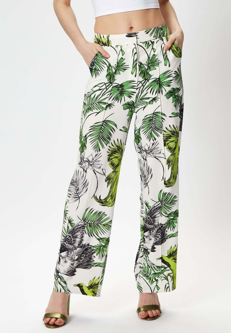 White wide-leg pants with green and black tropical leaf and bird print, featuring side pockets and a flat waistband.