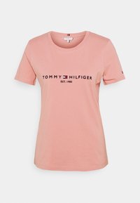 Camiseta de algodón rosa con mangas cortas, cuello redondo y un logo negro "TOMMY HILFIGER EST. 1985" en la parte delantera.