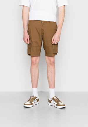 Braune Cargoshorts mit zwei Seitentaschen, Reißverschluss und leicht lockerem Schnitt, kombiniert mit weißen Socken und Sneakern mit braunen Akzenten.