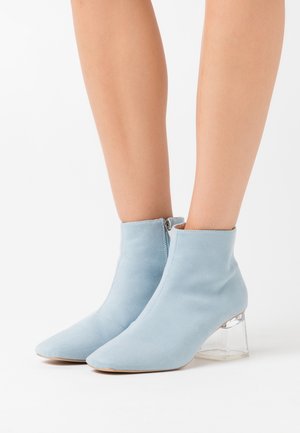 Stivaletti alla caviglia azzurri chiaro in morbido suede con punta appuntita e tacco a blocco trasparente, dotati di una cerniera laterale per la chiusura.