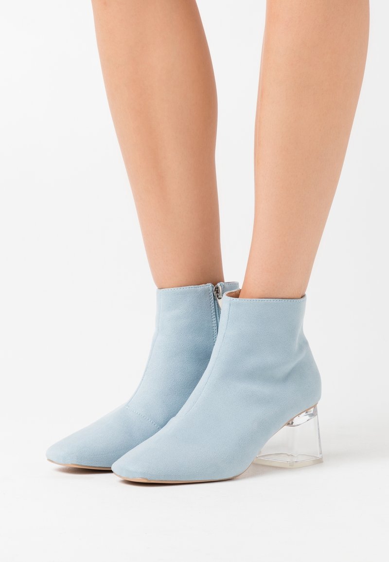 Hellblaue Stiefeletten aus weichem Wildleder mit spitzer Spitze und transparentem Blockabsatz, ausgestattet mit einem seitlichen Reißverschluss zum Verschließen.