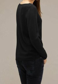 Svart långärmad stickad tröja med rund halsringning, figurnära silhuett och ribbad nederkant. Matchas med mörka jeans. Slät textur.