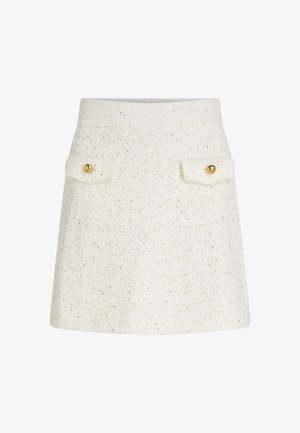 Bela teksturirana krila z diskretnimi zlatimi bleščicami, dvema sprednjima žepoma z zlatimi gumbi in tesnim pasom. Oblika se razširja navzdol.