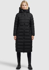 Fekete puffernadrág kapucnival, vízszintes steppelési mintával, elülső cipzárral és két oldalsó zsebbel. Fekete bokacsizmával párosítva.