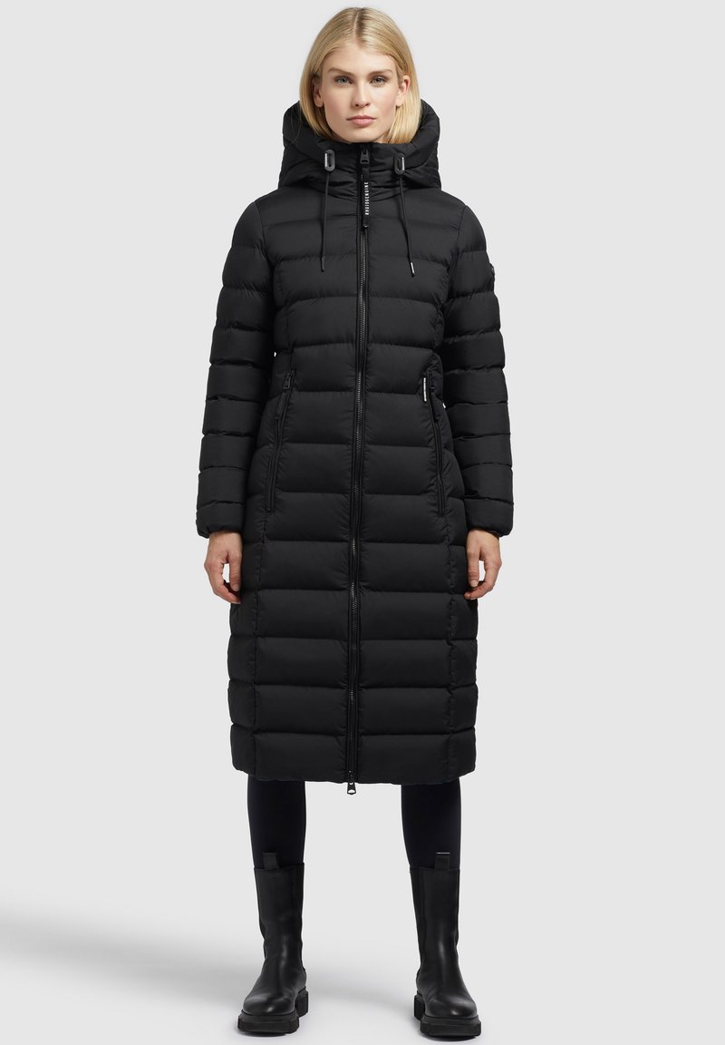 Fekete puffernadrág kapucnival, vízszintes steppelési mintával, elülső cipzárral és két oldalsó zsebbel. Fekete bokacsizmával párosítva.