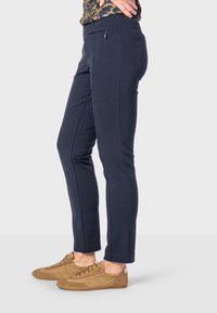 Navy slim-fit pants made of stretchy fabric, featuring side pockets and a smooth texture. Paired with brown suede sneakers.