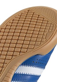 Semelle de chaussure de sport bleue avec une surface en caoutchouc gomme texturée et un motif carré proéminent, avec des accents blancs et des détails cousus.