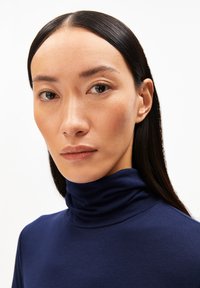 Navy-blaues Rollkragenoberteil aus weichem Material, mit hohem Kragen und figurbetontem Schnitt. Glatte Textur ohne sichtbare Muster.