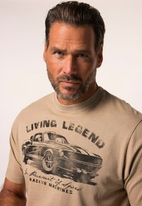 Camiseta de algodón beige con diseño impreso de un coche de época en negro, con el texto "LEYENDA VIVA" y "En Busca de Máquinas de Carrera Rápida."
