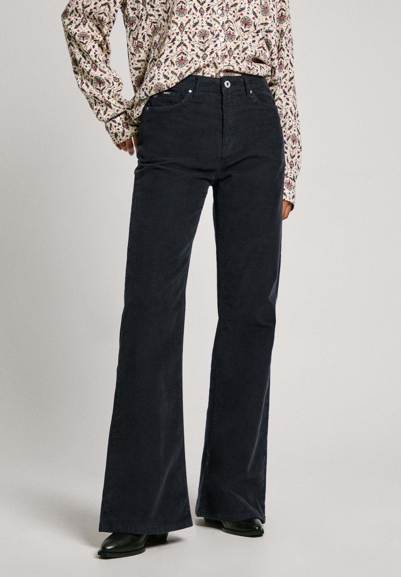 Pantalones de pana acampanados azul oscuro con un acabado texturizado, bolsillos frontales, pasadores para cinturón y cierre de botón metálico.