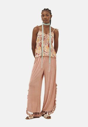 Top ligero con estampado floral en melocotón y crema, combinado con pantalones sueltos de color rosa pálido que presentan flecos en los dobladillos.