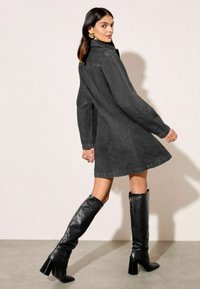 Musta farkkumekko pitkähihaisilla, levenevällä helmalla, takataskuilla ja kauluksella. Yhdistetty polvipitkiin mustiin nahkabootseihin ja minimaaliseen koruvalintaan.