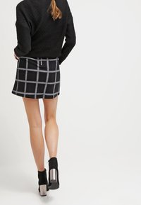 Minifalda de cuadros en blanco y negro con un diseño ajustado, tejido texturizado y cierre de cremallera en la parte trasera, complementada con botas hasta el tobillo con acentos metálicos.
