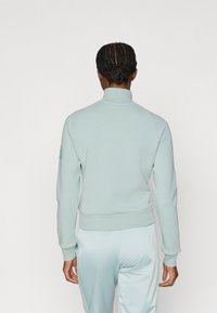 Světlě modrá mikina s vysokým límcem, vyrobená z měkkého materiálu. Má žebrované manžety a lem, s čistým, minimalistickým designem.