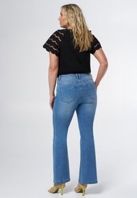 Haut noir avec des manches en dentelle, jeans évasés bleus, délavés avec des poches, et sandales à talons jaunes. Mettez l'accent sur les textures et les détails de conception.