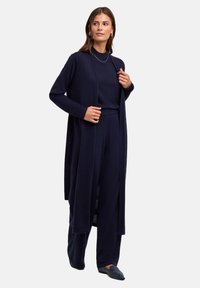Granatowy długi kardigan z otwartym przodem, noszony na pasującej bluzce i spodniach. Miękka, teksturowana tkanina o luźnym kroju i minimalistycznym designie.