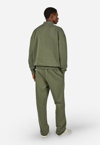 Zaļš džemperis un saskaņotas sportiskās bikses, kas izgatavotas no mīksta materiāla, piedāvā augstu apkakli, brīvu piegriezumu un ribota tipa aproces.