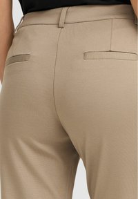 Pantaloni beige su misura con una finitura liscia, dotati di due tasche posteriori e una vita aderente.