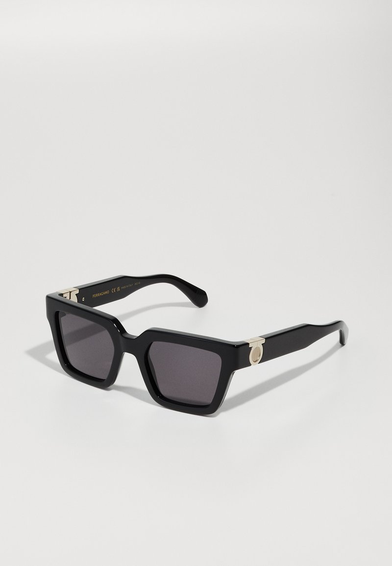 Black square sunglasses with dark lenses. Features gold-tone hardware accents on the temples. Bold, thick frame design with a smooth finish.
